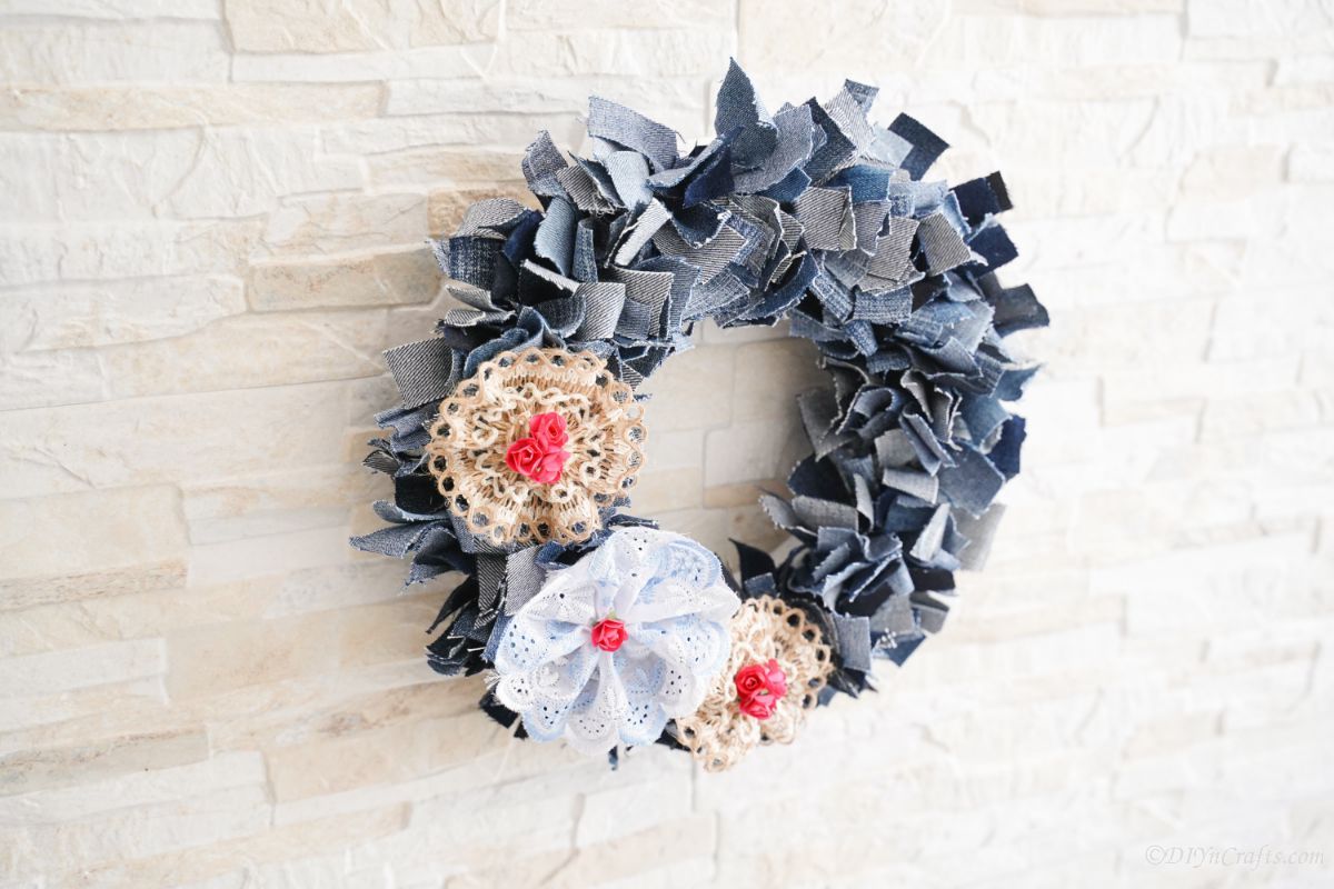 lace flowers on side of denim rag wreath hanging on brick wall