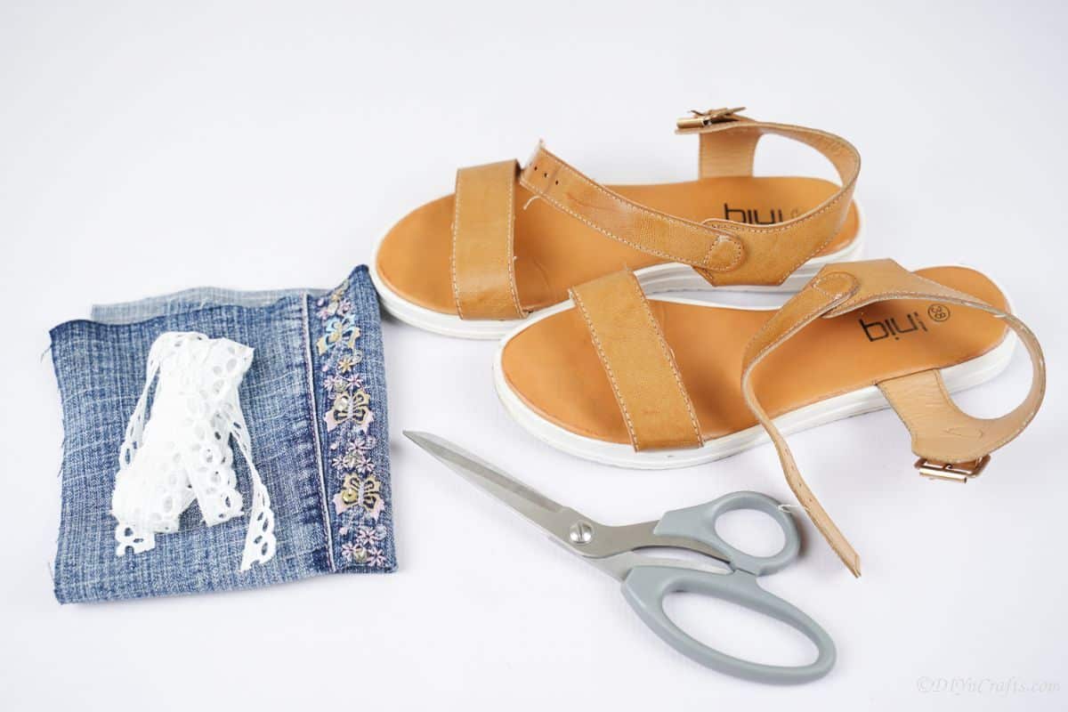 brown sandals on white table with folded jeans scissors and lace