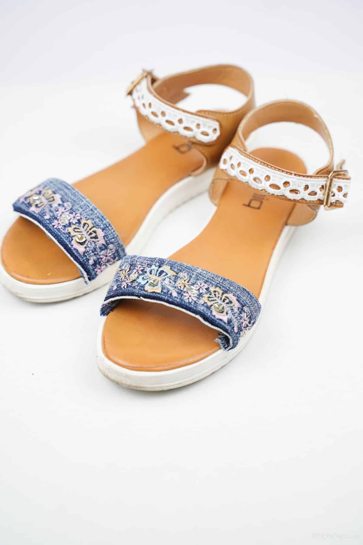 brown sandals with denim and lace straps on white table