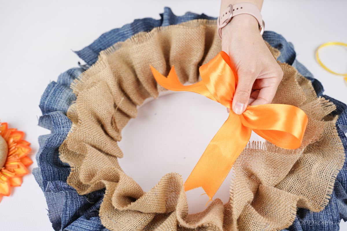 hand holding orange ribbon bow above wreath