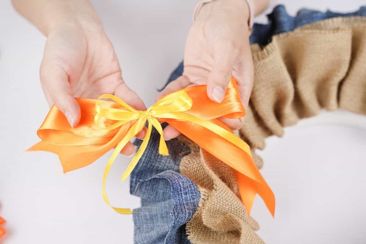 small yellow bow on top of orange bow above burlap and denim wreath
