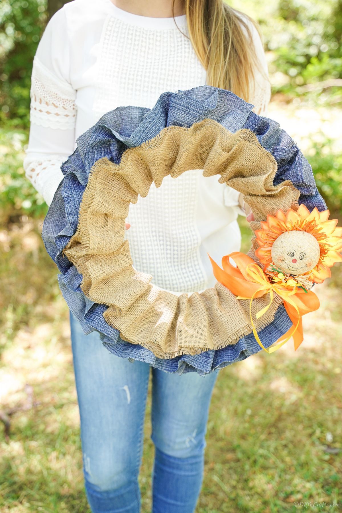 woman in white shirt and jeans holding denim and burlap wreath