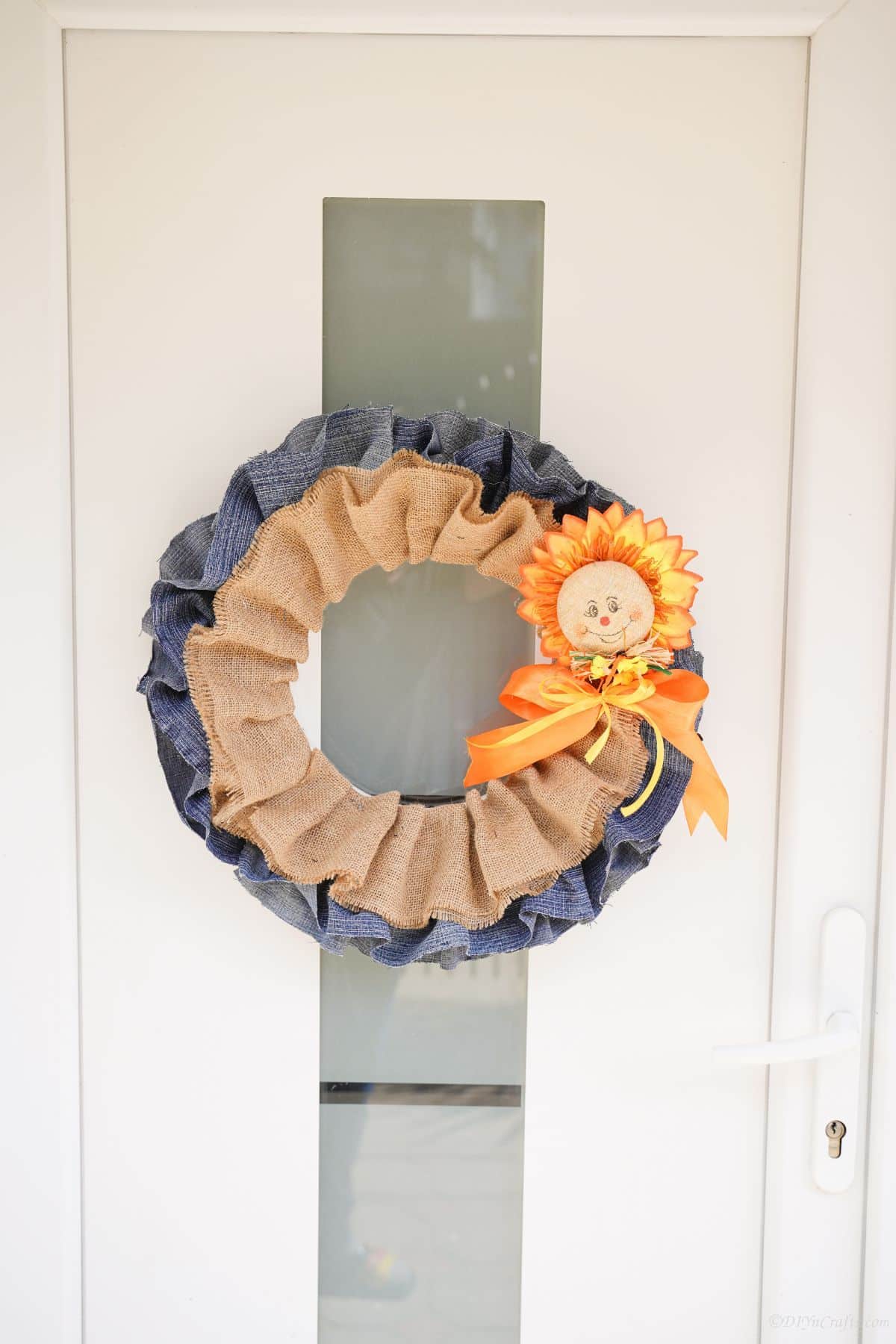 denim and burlap wreath hanging on white door with glass panel