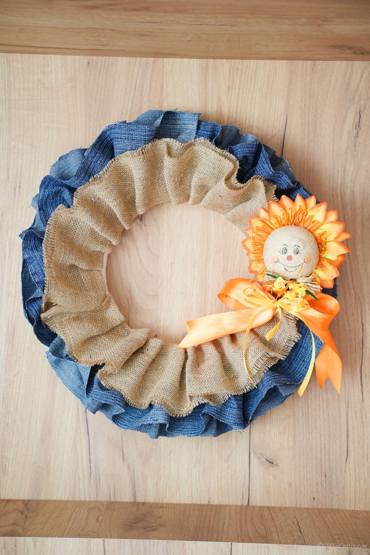 denim and burlap wreath on wood wall with small scarecrow on side