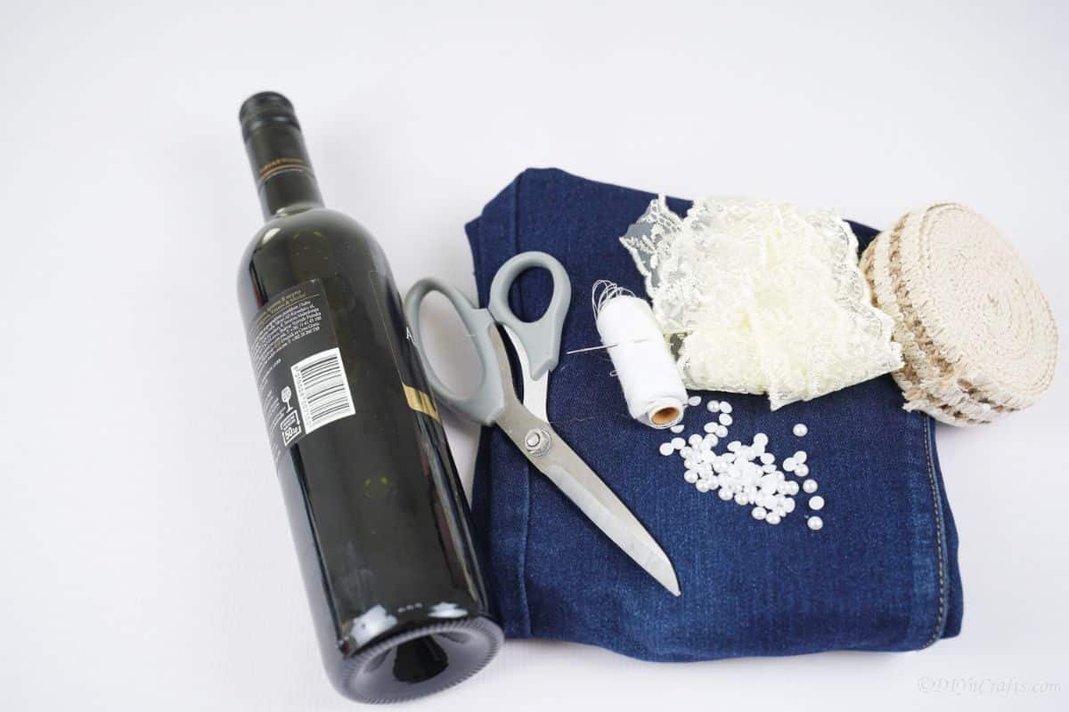 blue jeans wine bottle scissors and beads on white table