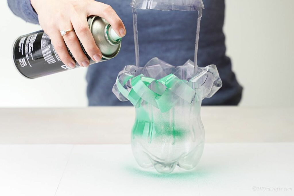 hand spraying green paint onto plastic bottle planter