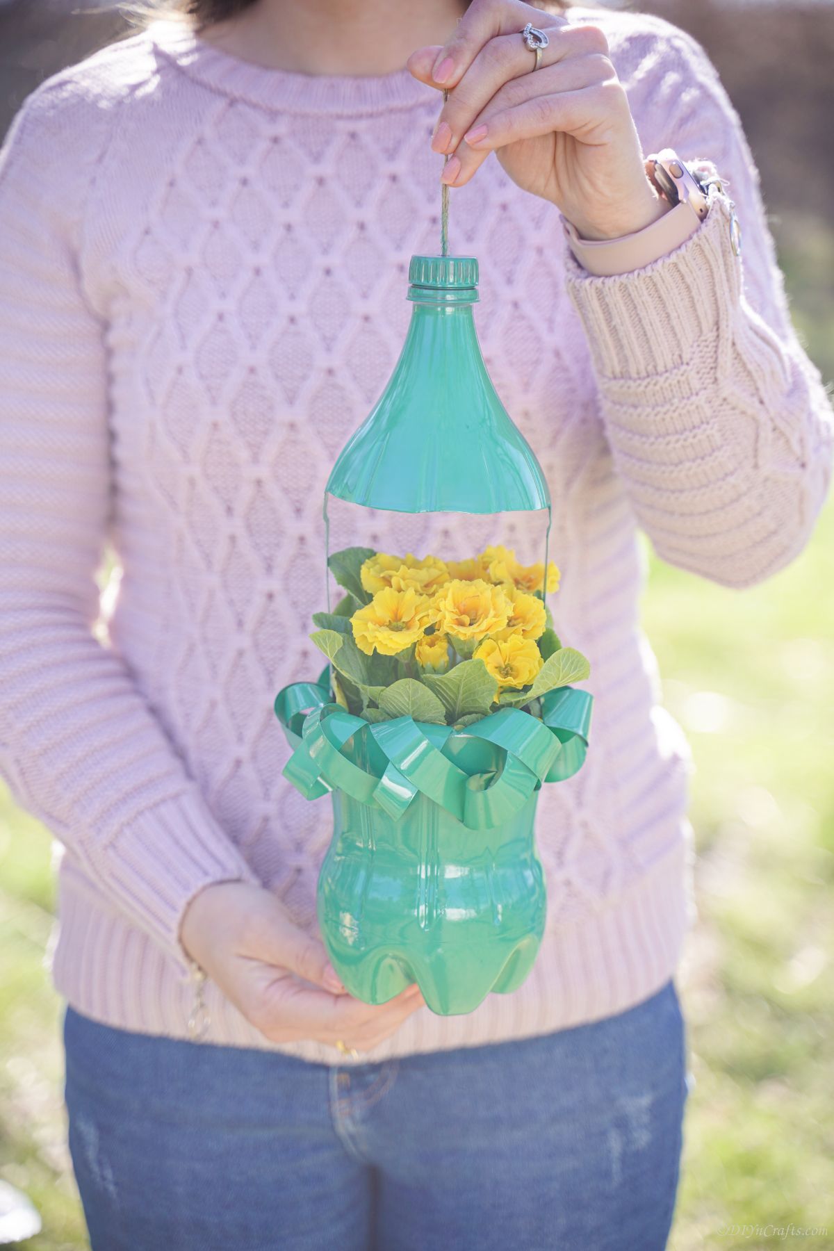 green bottle planter with yellow flowers held by woman in pink