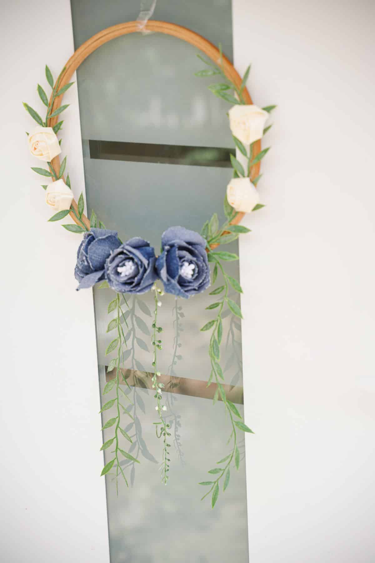white rose and denim flower wreath hanging on white door with glass panel
