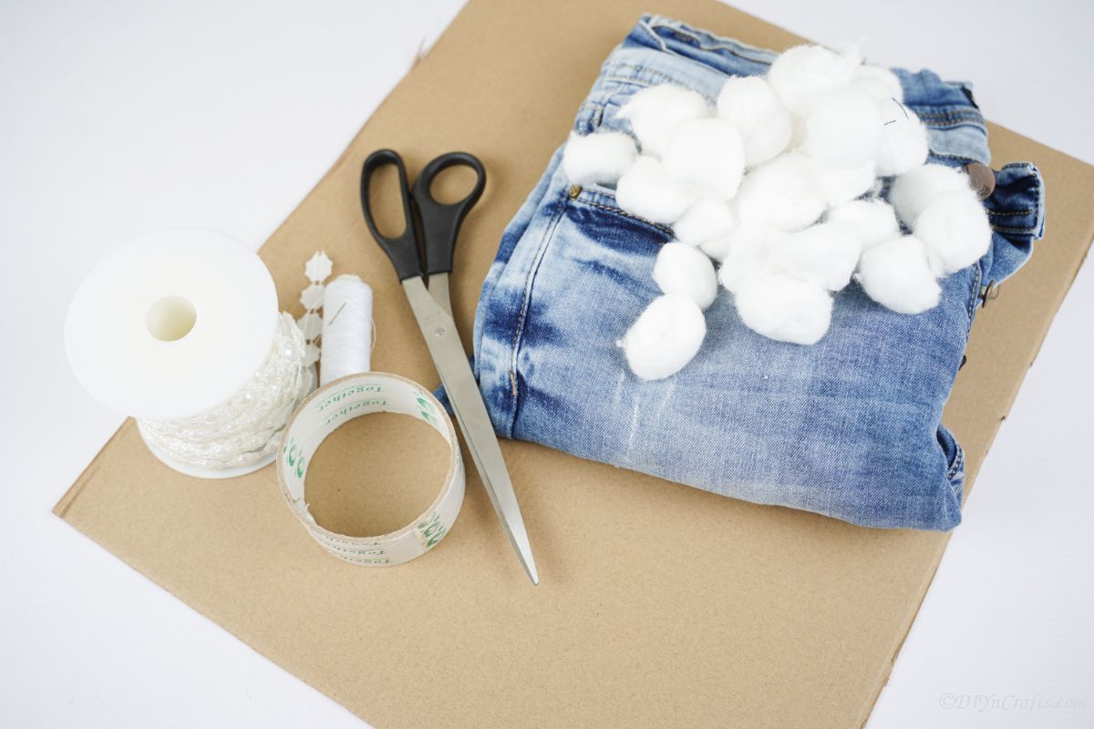 cardboard on table with blue jeans scissors and cotton balls on top