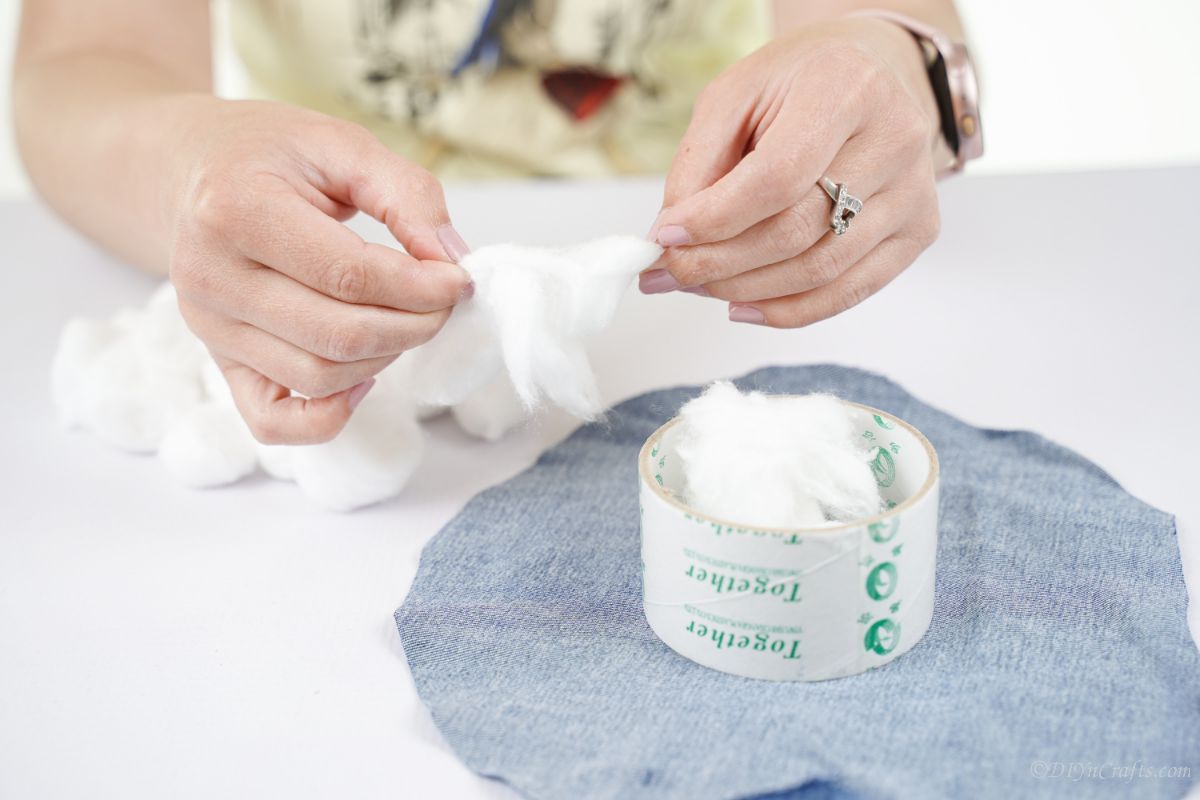 hand pulling apart cotton ball and putting inside circle on denim