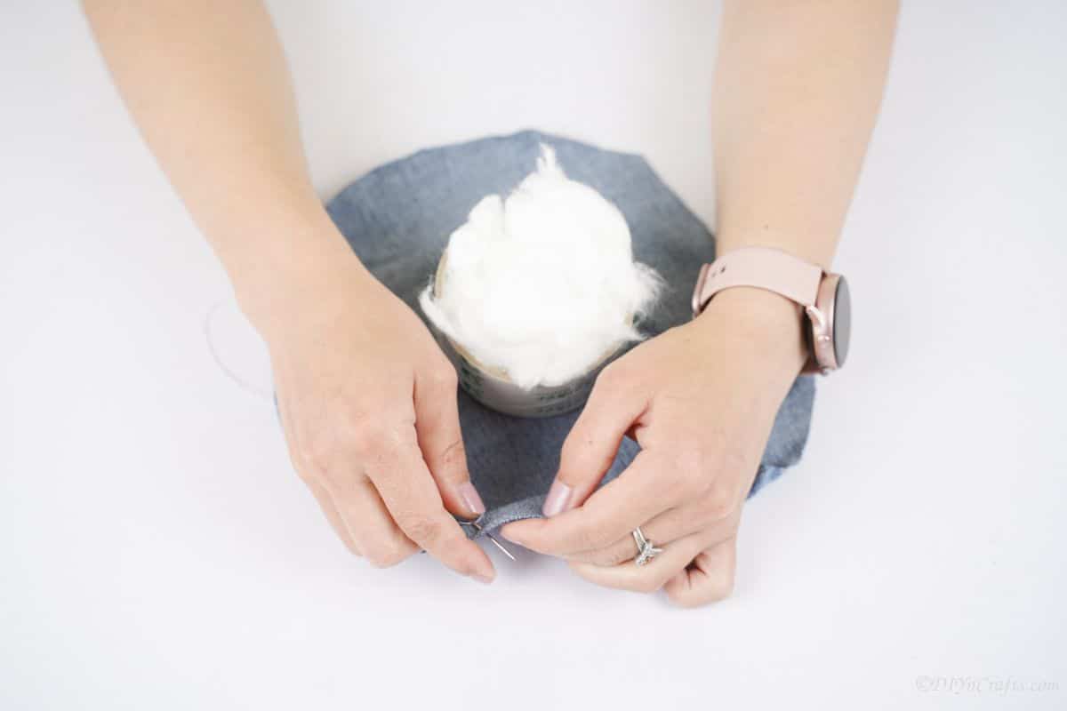 hand sewing edge of denim around bundle of cotton