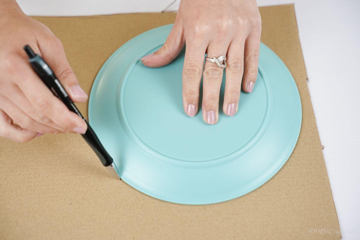 hand tracing around plate on cardboard