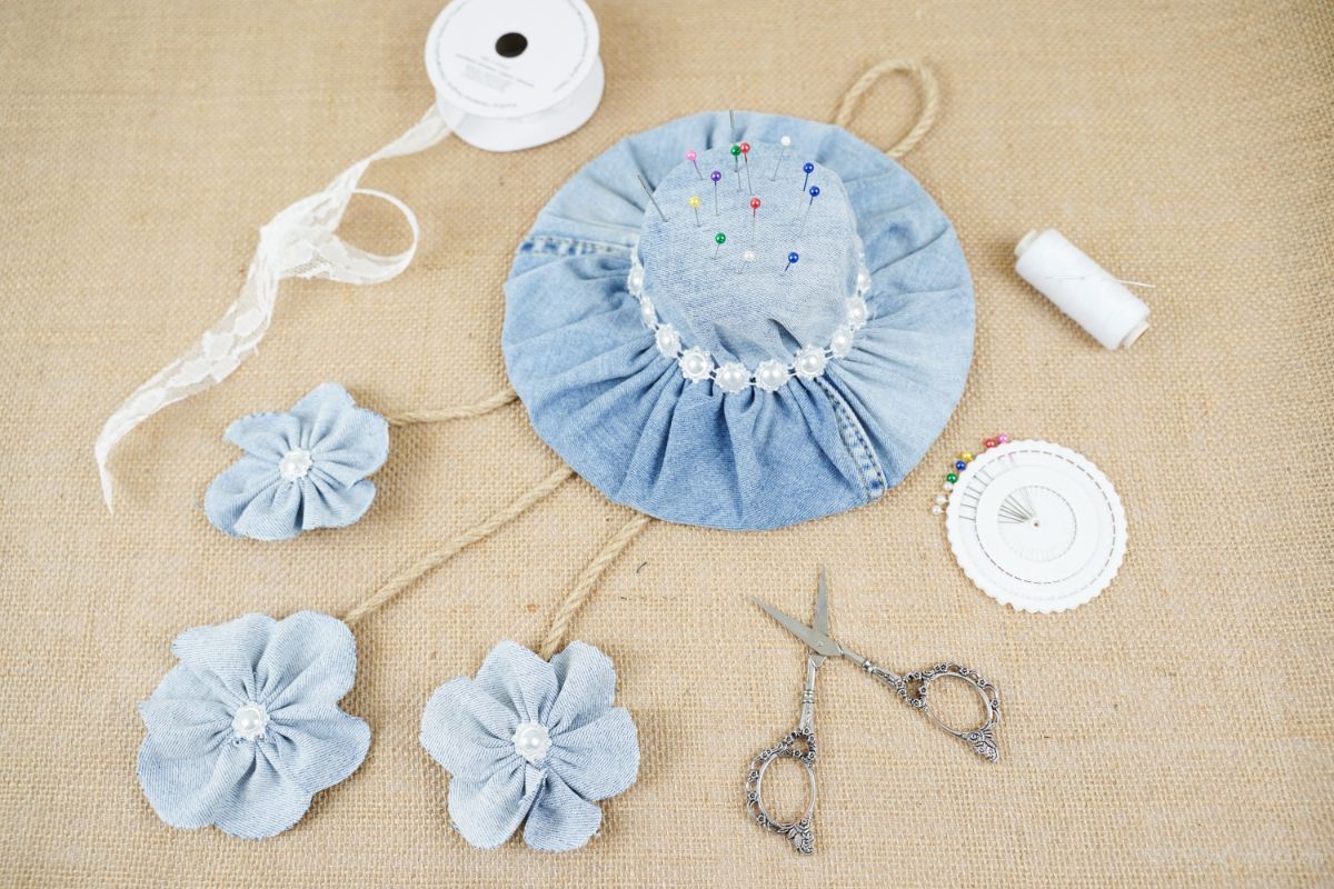 denim hat pin cushion on brown surface with scissors and spools of thread