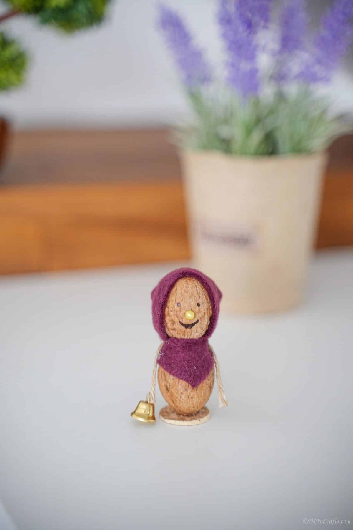 walnut mouse with purple bonnet on white table with plant in background