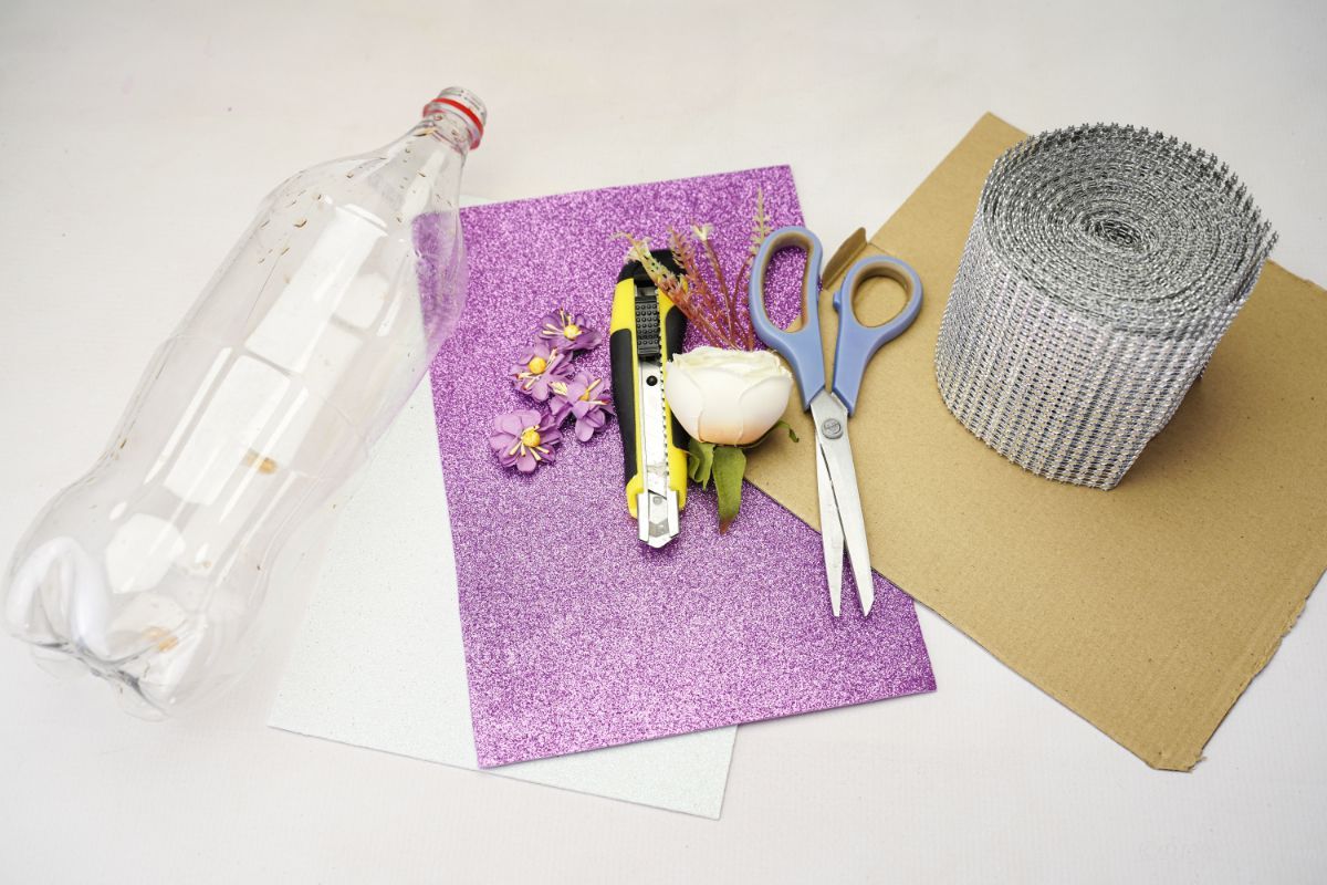 lila glitterpapper plastflaska kartong och sax på vitt bord