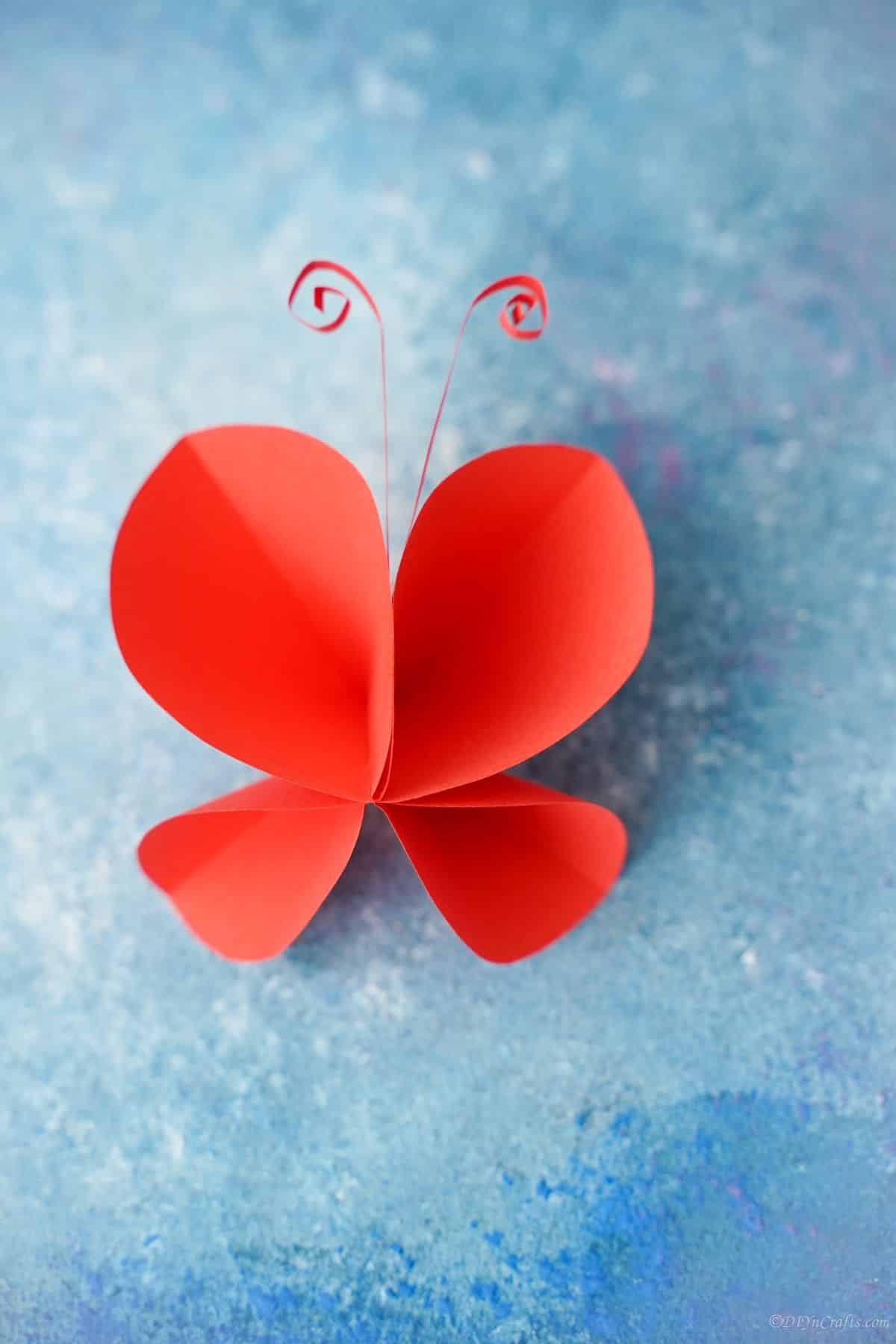 red paper butterfly underneath blue paper