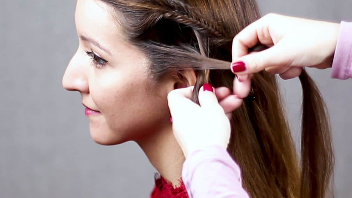 hand with red nails braiding small piece of hair above ear on brunette