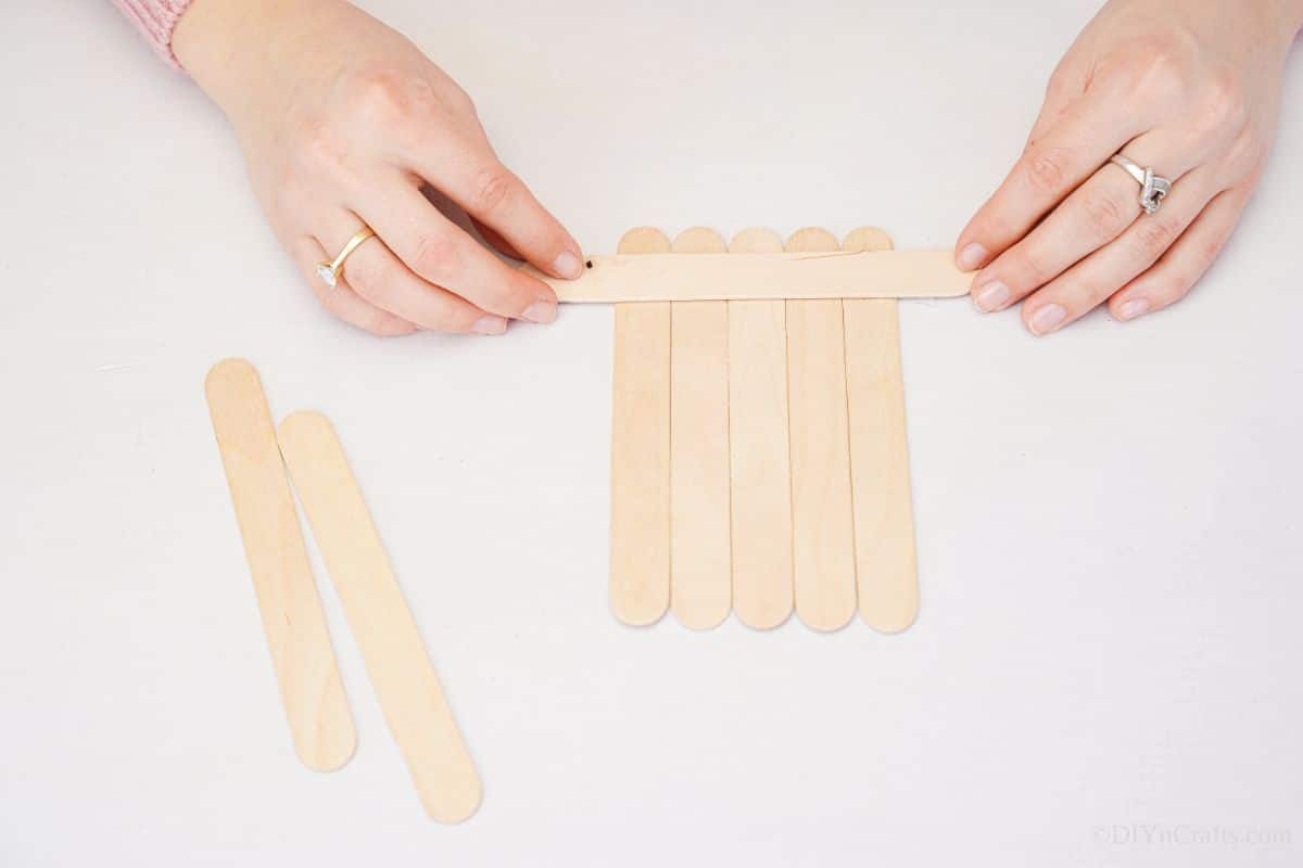hand placing craft sticks together on table