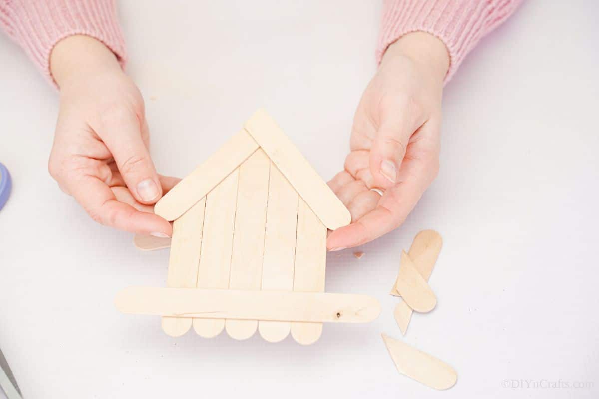 hand holding craft stick house above white table