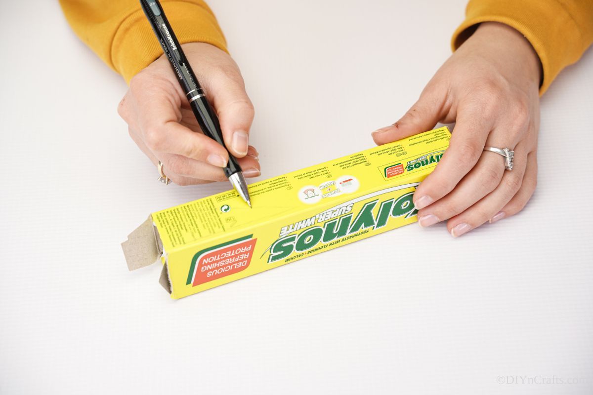hand using pen to mark on side of empty toothpaste box