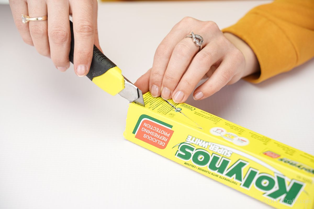 craft knife cutting into empty toothpaste box