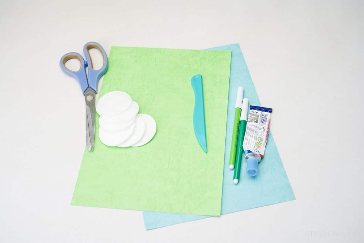 blue and green paper on table with scissors and glue