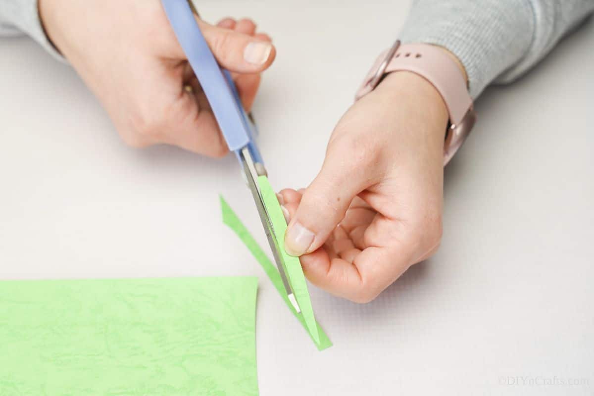 hand cutting green paper with blue scissors