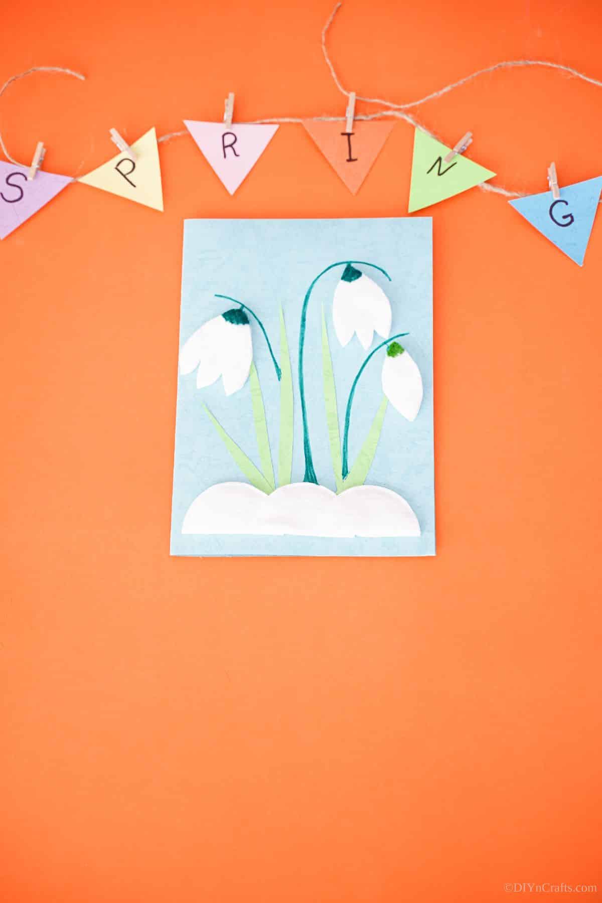 blue tulip handmade card laying on orange paper with spring sign