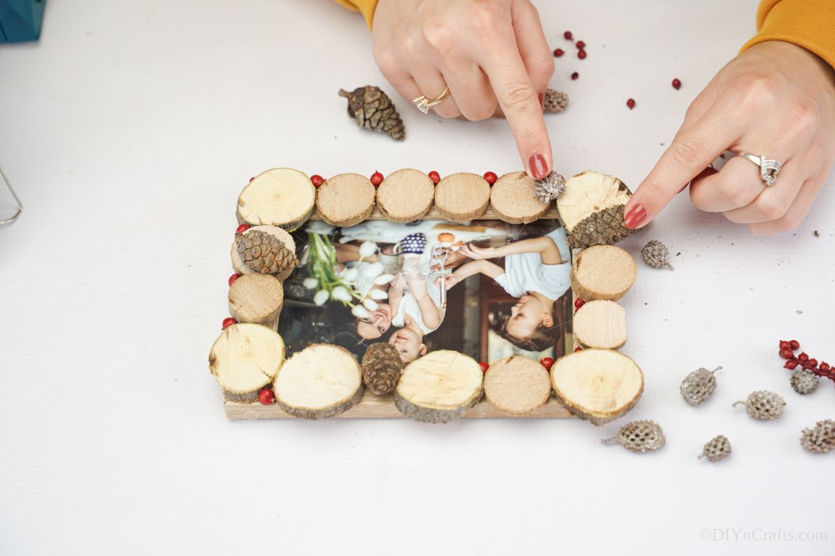 hand adding mini pinecones to side of wood slice picture frame