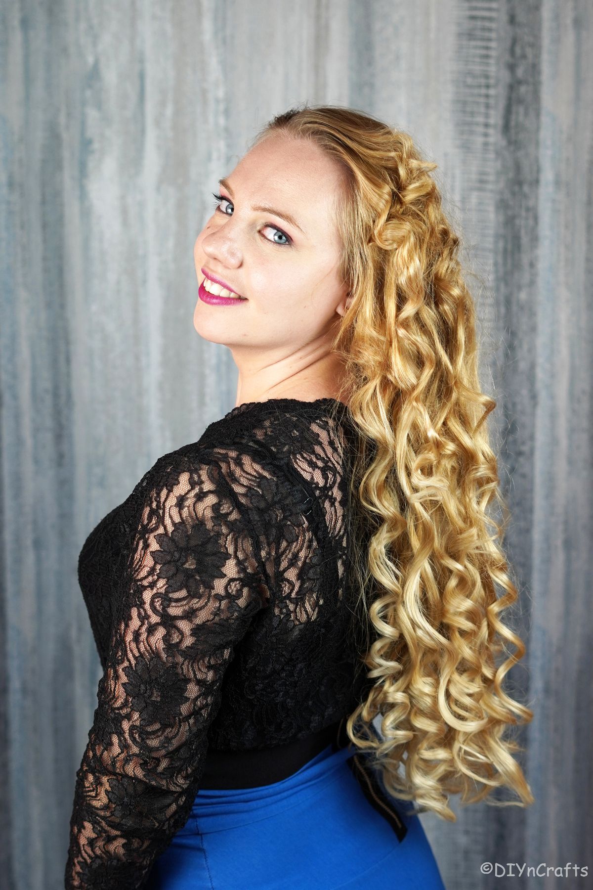 woman looking over her shoulder wearing a black lace shirt with long blonde curls