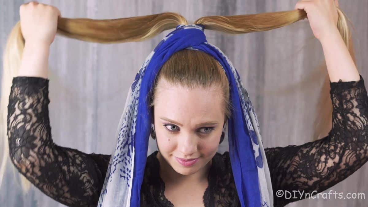 woman dividing hair of ponytail above scarf