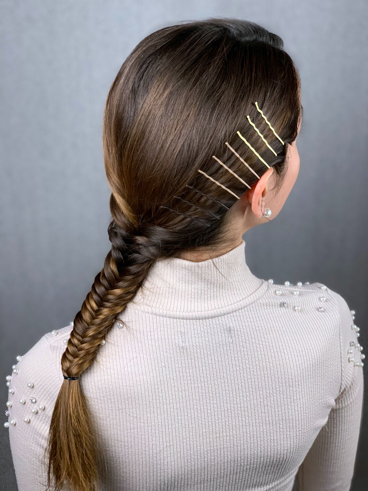 back of bobby pin hairstyle with fishtail braid on woman in pink sweater