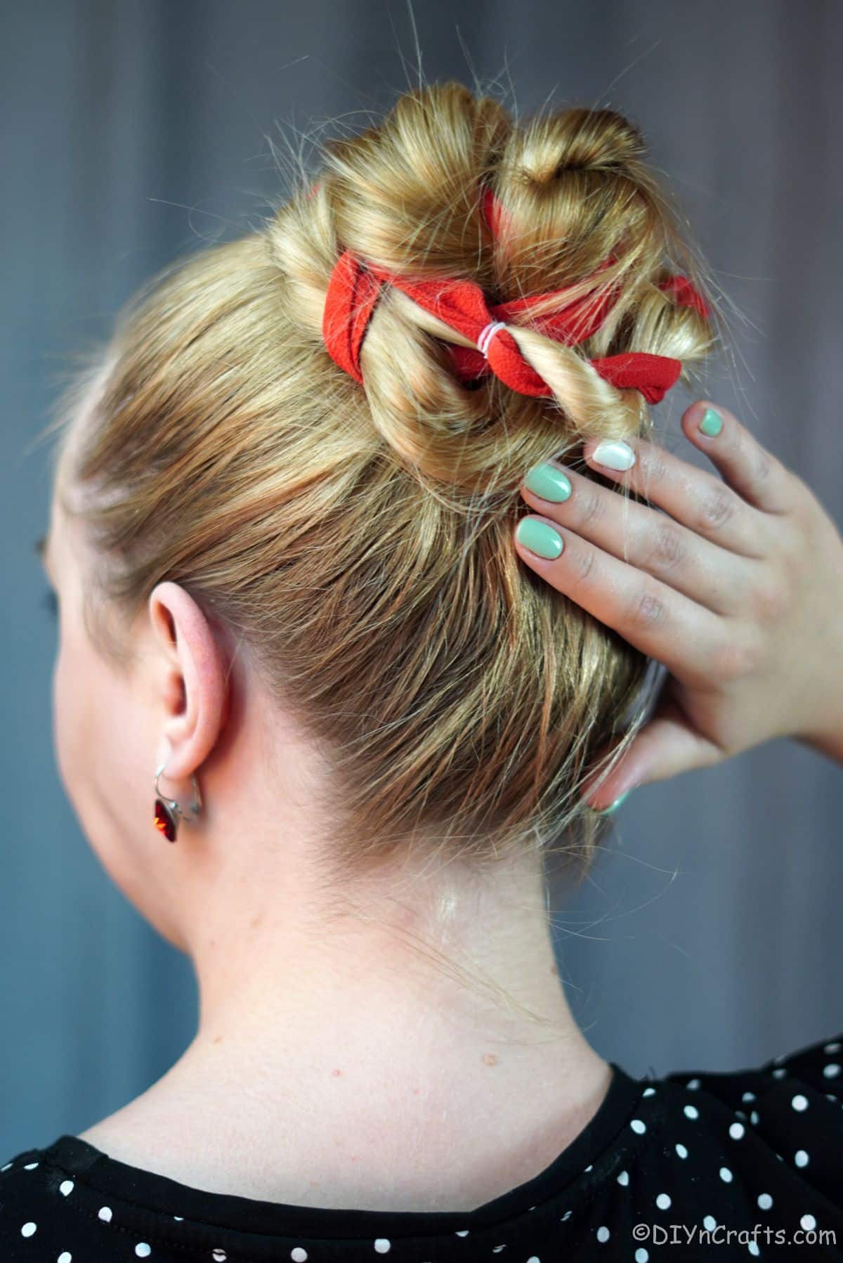hand with green painted nails against red ribbon high twisted bun