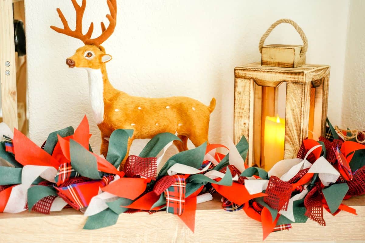 Fake deer and lantern on shelf with colorful Christmas rag garland in front