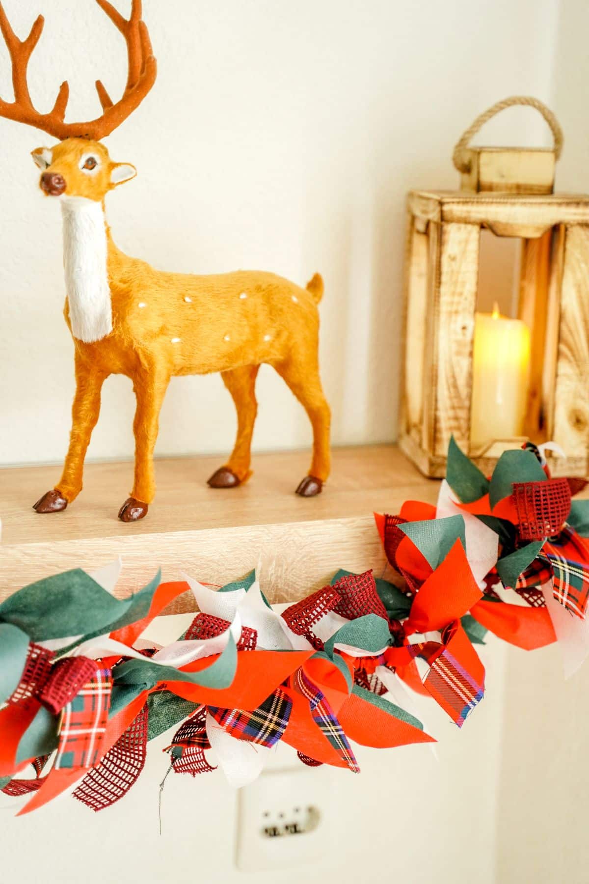 red, green, and white fabric garland hanging on shelf by fake deer and lantern