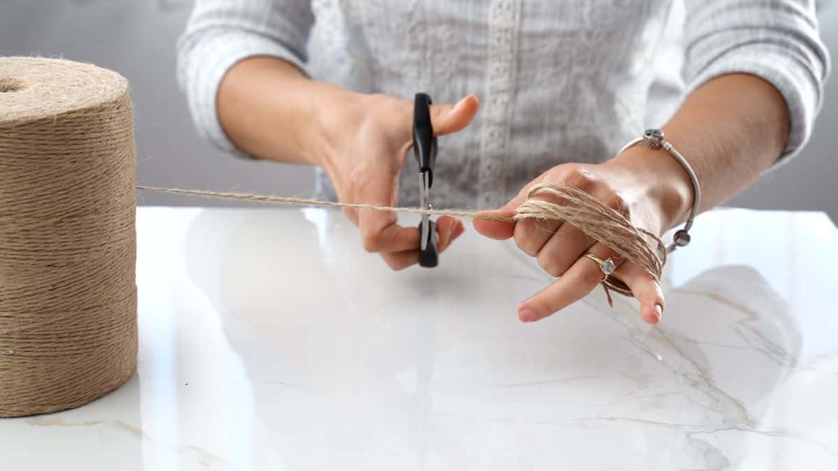 hand holding roll of twine and cutting length with scissors
