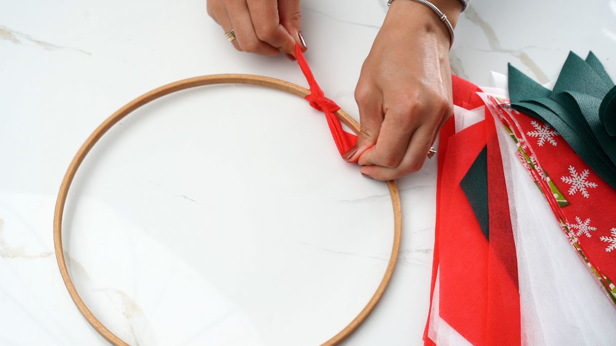 hand tying red ribbon onto wreath form