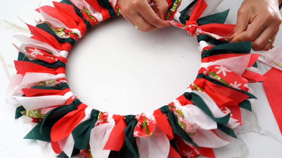 tying colorful holiday ribbon on wreath form