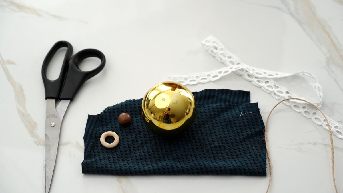gold ornament on top of green fabric by lace and a pair of scissors on marble table