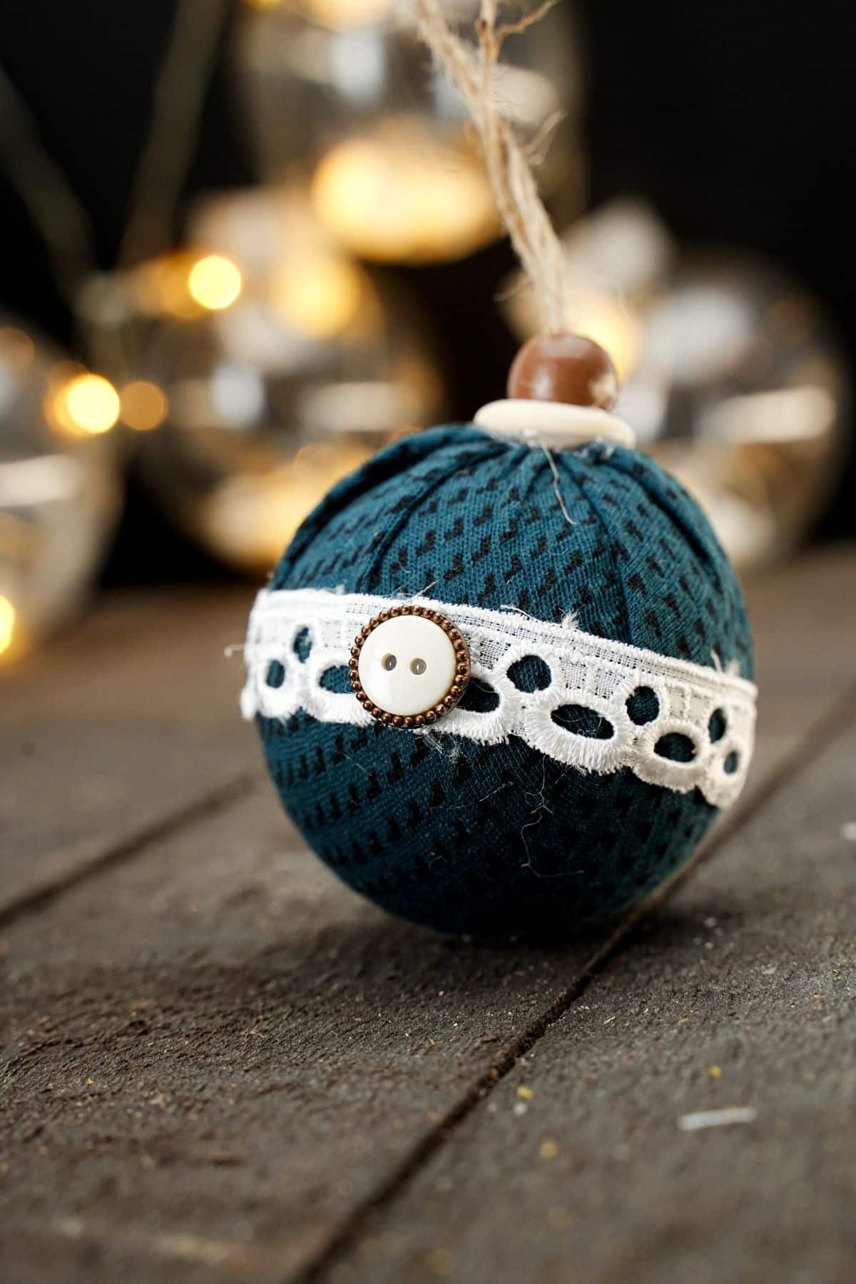 fabric ball ornament on wood table with lights in background