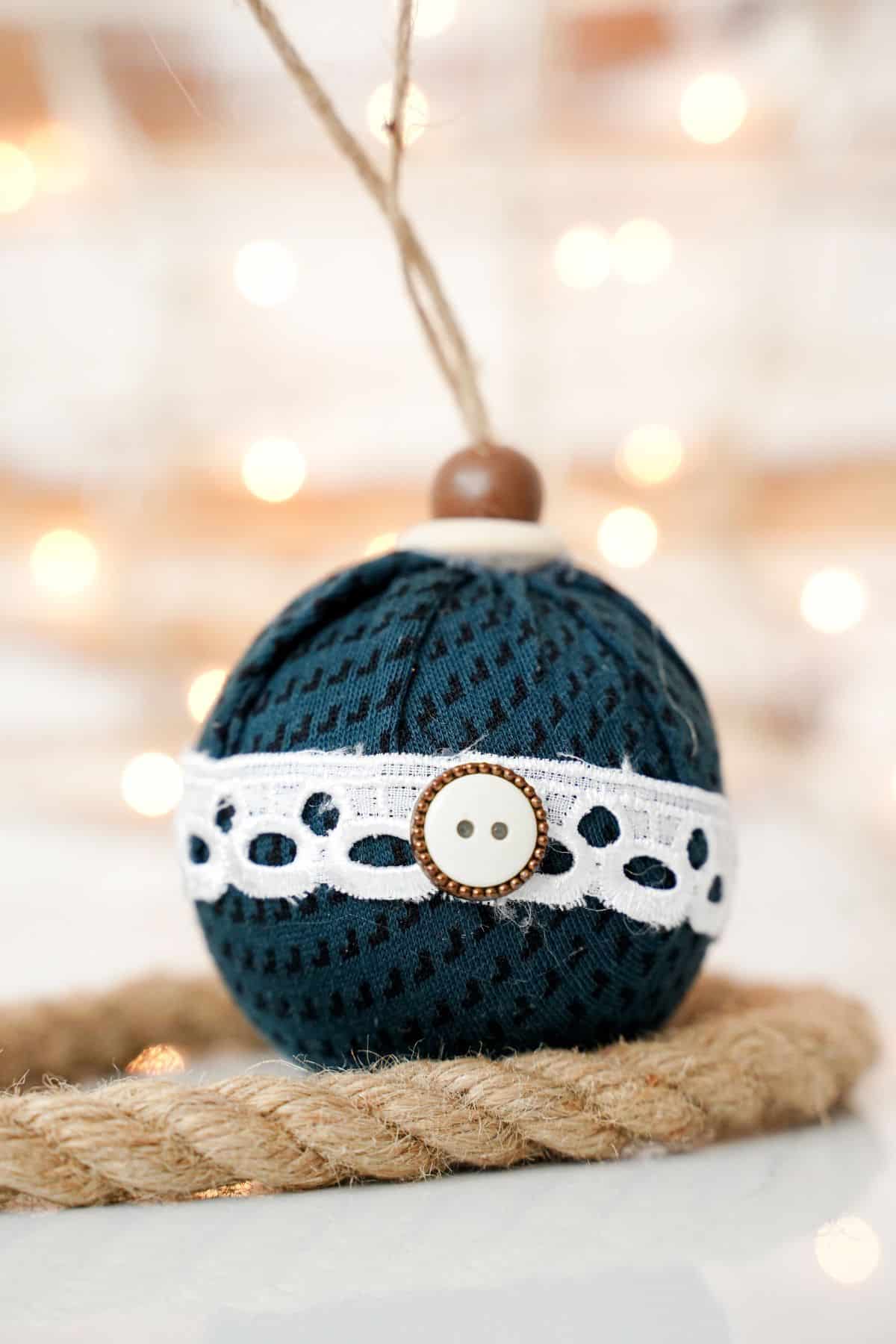 rope under fabric ball ornament on table with lights in background