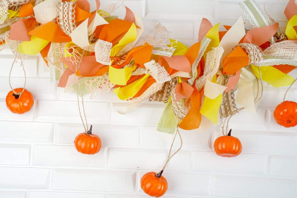 mini pumpkins hanging down against white wall from fall rag garland