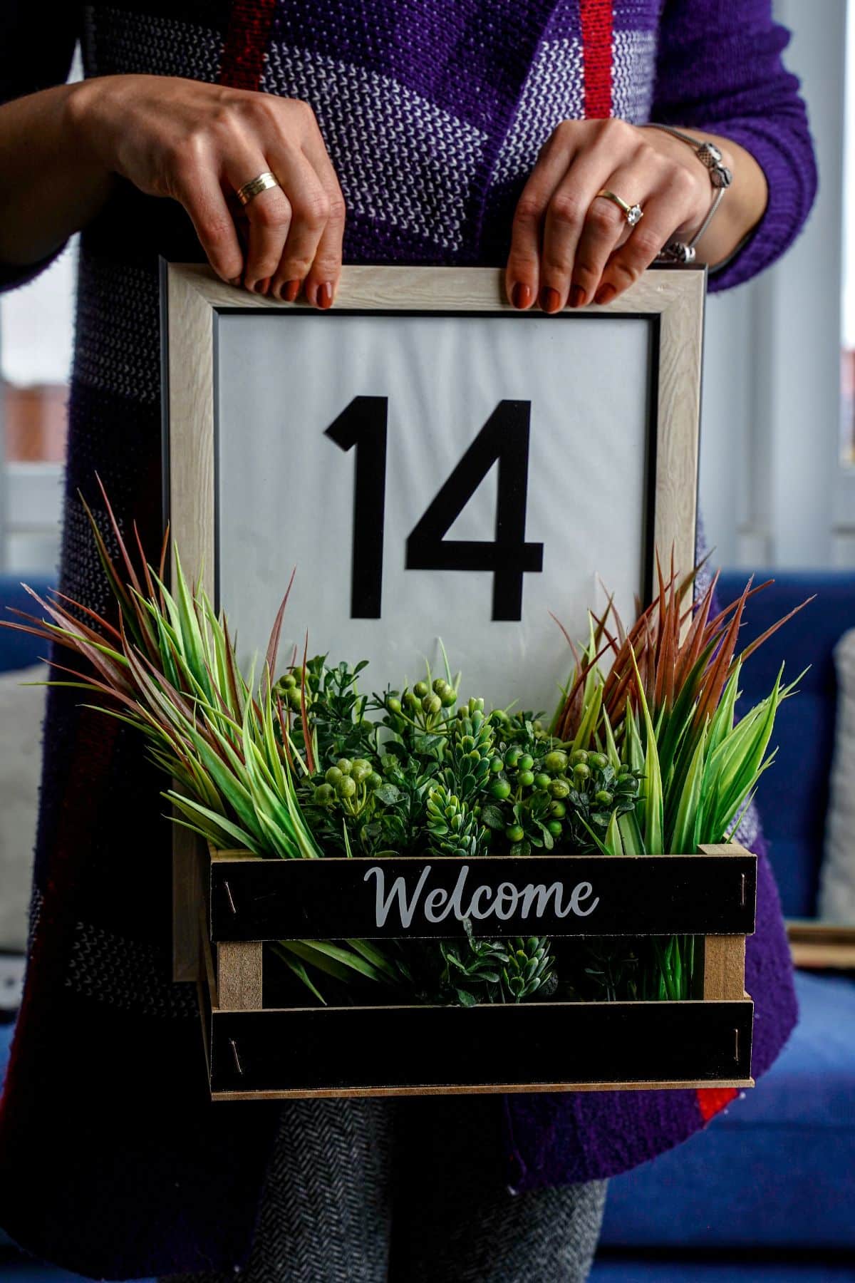 woman in purple holding framed house number sign